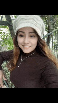 a woman wearing a white hat and a brown sweater smiles for the camera