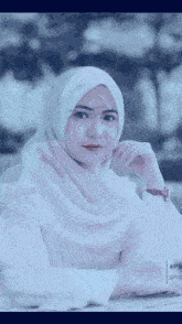 a woman wearing a white hijab is sitting at a table with her hand on her chin