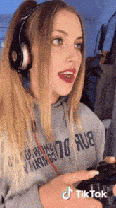 a woman wearing headphones and a hoodie that says 70 aub is holding a video game controller