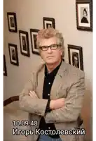 a man wearing glasses and a plaid jacket is standing with his arms crossed in front of a wall of pictures
