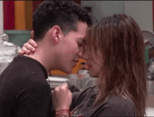 a man and a woman are kissing in a kitchen in front of a colorful background .