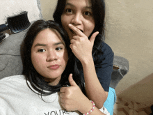 a girl giving a thumbs up next to another girl who is wearing a shirt that says youre