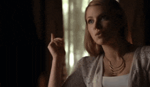 a woman wearing a white sweater and a gold necklace is pointing upwards