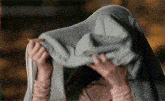 a woman covering her face with a blanket while holding a pencil