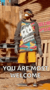 a man in a colorful hoodie and yellow shorts is standing in front of a building and says `` you are most welcome '' .