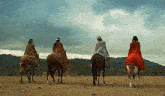 a group of people riding horses in a field with mountains in the background