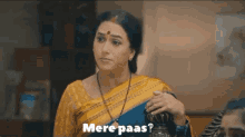 a woman in a yellow saree is holding a purse and says mere paas .
