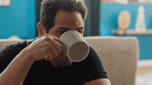 a man in a black shirt is drinking from a white coffee mug