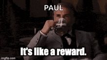 a man in a suit and tie is holding a glass of beer and says paul it 's like a reward