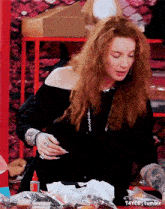 a woman with long red hair is sitting at a table with a bottle of glue .