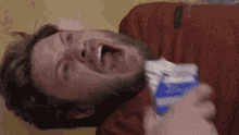 a man with a beard is laying on his back with his mouth open and holding a bag of milk .