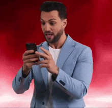 a man in a blue suit is looking at his cell phone with a surprised look on his face
