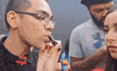 a man with glasses is applying lipstick to a woman 's face