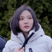 a woman with purple hair is wearing a white jacket and looking at the camera .