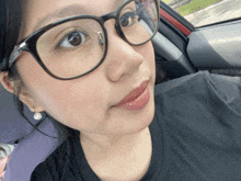 a woman wearing glasses and a black shirt is in a car