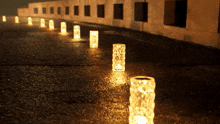 a row of candles are lit up on a wet sidewalk