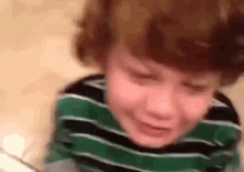 a young boy in a green and black striped shirt is crying and making a funny face .