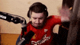 a man wearing headphones and a red shirt is standing in front of a microphone .