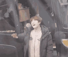 a young man in a jacket is waving his hand in front of a truck that says 12.5 m on it .