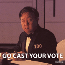 a man in a tuxedo with the number 100 on his chest says " go cast your vote "
