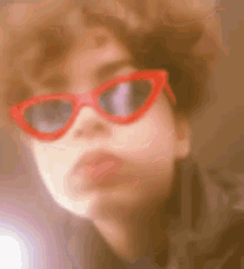 a woman wearing red sunglasses is looking at the camera .