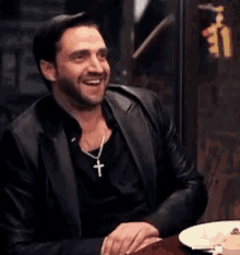 a man in a black jacket is sitting at a table with a plate of food .