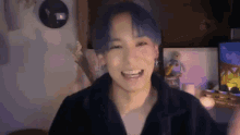 a young man with blue hair is smiling and waving in a room .