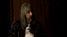 a man with long blonde hair is sitting on a black leather couch and talking on a cell phone .