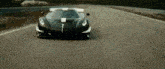 a black sports car is driving down a road with trees in the background