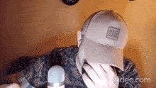 a man wearing a hat is sitting in front of a microphone and covering his face .