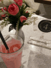 a glass of pink liquid sits on a table next to a vase of flowers