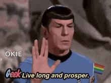 a man in a blue shirt is holding a small rainbow flag and says geek live long and prosper .
