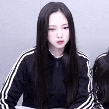a girl with long black hair wearing a black jacket with white stripes on the sleeves