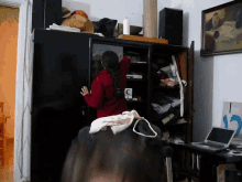 a woman in a red jacket is standing in a messy room with a sign that says 12
