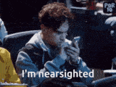 a man sitting in a theater looking at his phone with the words " i 'm nearsighted " above him