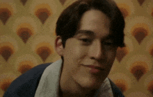 a young man is smiling and looking at the camera in front of a patterned wallpaper .