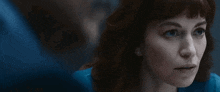 a woman with red hair and blue eyes is looking at herself in a mirror .