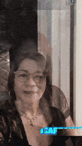 a woman wearing glasses and a necklace is standing in front of a sign that says " i & af "