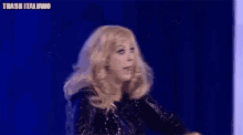 a woman wearing a wig and a black dress is standing in front of a blue background .