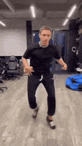 a man in a black t-shirt and black pants is dancing in a room .