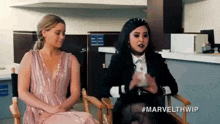 two women are sitting in chairs talking to each other in an office .