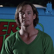 a man in a green shirt is standing in front of a scooby doo vehicle .