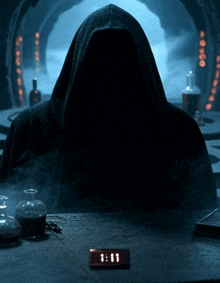 a man in a hooded cloak sits at a table with a clock that reads 8:01