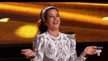 a woman in a white dress is standing on a stage with her arms outstretched and smiling .