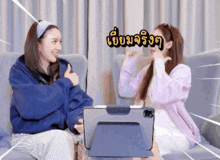 two women are sitting on a couch and one is holding a tablet and the other is holding her hand up
