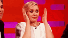 a woman is making a funny face while clapping her hands in front of a red background .
