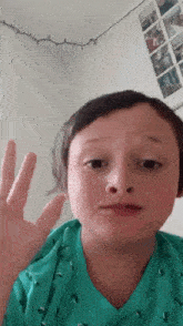 a young boy in a green shirt is making a funny face with his hand .