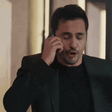 a man in a black suit is talking on a cell phone .