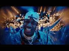a man wearing a hat and a necklace is smiling in front of a crowd of lights .