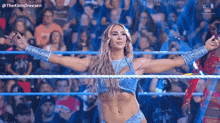 a female wrestler is standing in a wrestling ring with her arms outstretched in front of a crowd .